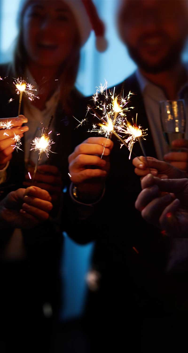 Group of colleagues with flutes holding Bengal lights during holiday party  Group of colleagues with flutes holding Bengal lights during holiday party<br />
