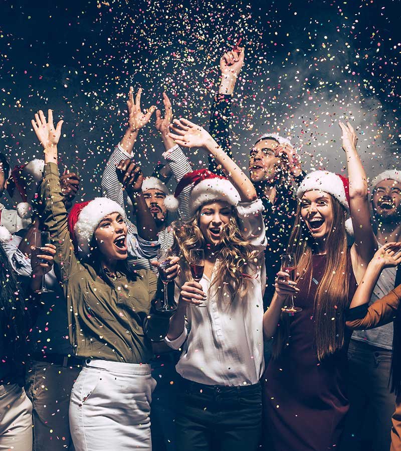 group of young people in Santa hats throwing colorful confetti, drinking champagne, and dancing over a gray background  group of young people in Santa hats throwing colorful confetti, drinking champagne, and dancing over a gray background<br />